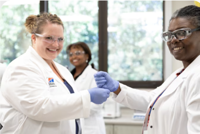Dos científicos con batas de laboratorio y guantes sonríen y se estrechan la mano en un entorno de laboratorio.